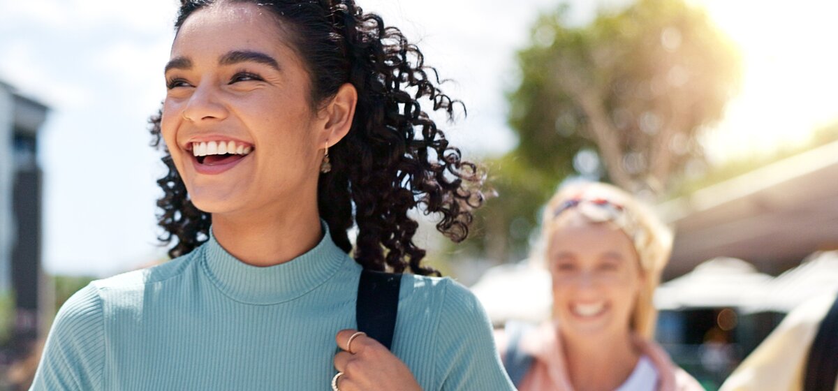 Frau mit lockigem Haar und blauem Rollkragenpullover trägt Rucksack im Freien bei sonnigem Wetter.